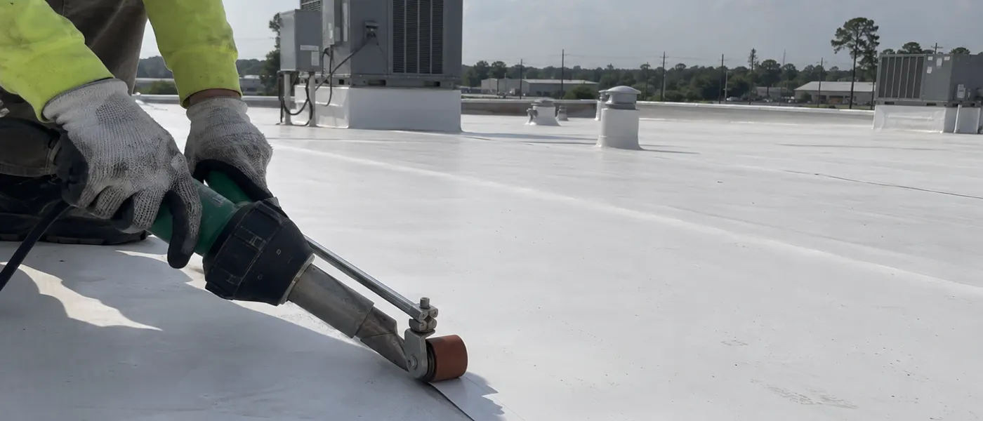 Sample photo: a roofer heat-welding the seam of a white TPO roof on a commercial building.