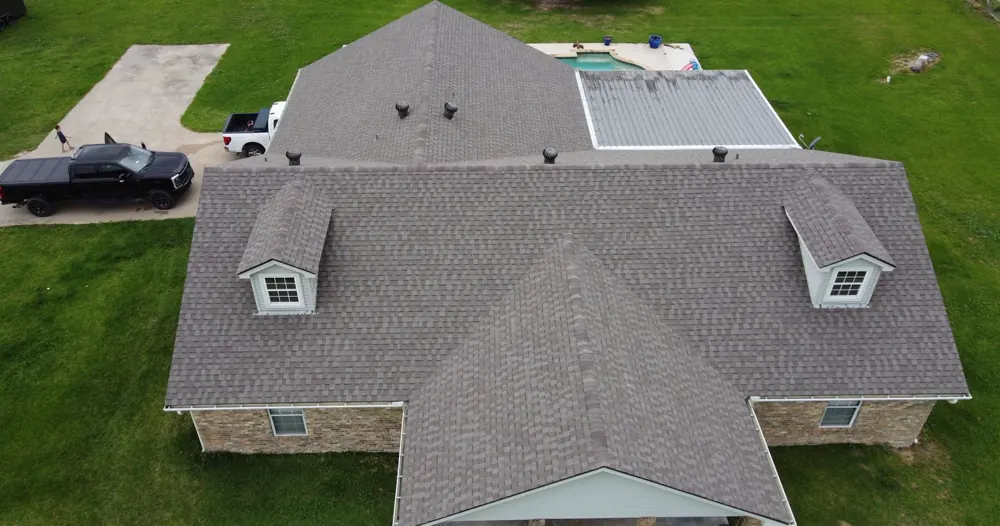 Drone view of a grey shingle roof with two dormers and a pickup in the drive.