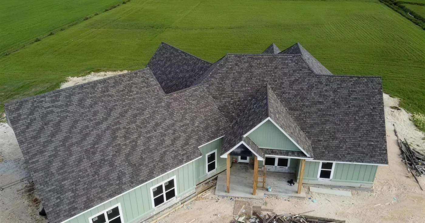Drone view of a new house with green siding and a fresh shingle roof, building debris still in the yard.